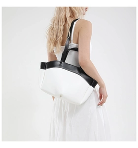 Detail of minimalist black and white tote bag worn by a model in a white dress