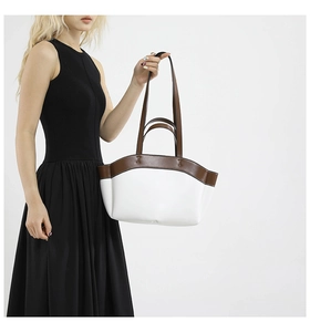 Detail of white leather tote bag with brown trim and dual handles on a model