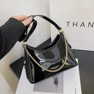 Glossy black patent leather trapezoid handbag with gold chain and wide shoulder strap