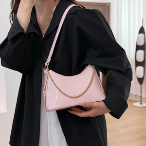 Pink patent leather crescent shoulder bag with gold chain worn on a black shirt