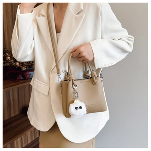 Detail of khaki bucket bag featuring knotted handle and cute white plush ball ornament