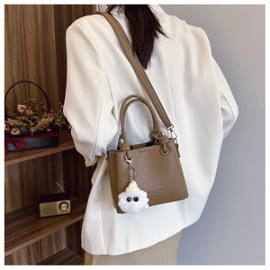 Detailed view of a brown pebbled leather bucket bag with a cute plush monster charm