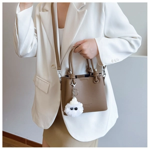 Close-up of brown litchi pattern leather bucket bag with cute white plush monster charm