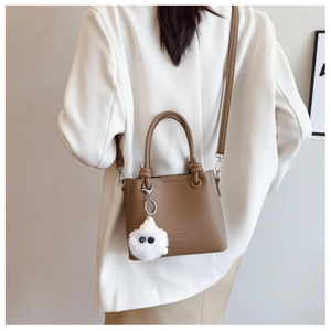 Litchi texture brown bucket bag with plush monster charm worn by a model in a white suit