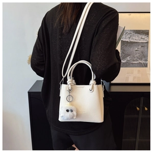 Detailed view of white litchi pattern bucket bag with a cute plush monster charm