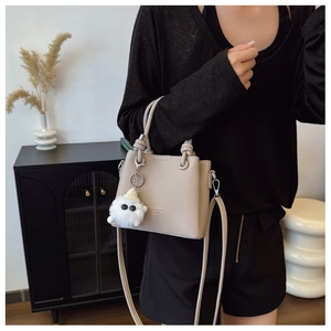 Detail of khaki lychee grain bucket bag with knot handle and cute monster plush charm