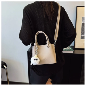 Detail of beige lychee texture bucket bag with plush monster charm and adjustable strap