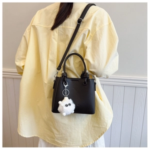 Detail of black pebbled leather bucket bag with cute white plush monster charm accessory
