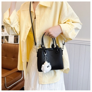 Detail of black lychee grain leather bucket bag with cute white pompom charm
