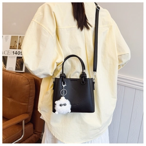 Rear view of a black lychee texture bucket bag with a white plush ball charm on a model