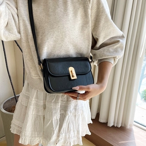 Minimalist black leather square crossbody bag with gold buckle on a fashion model