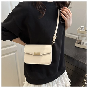 Modèle portant un sac bandoulière carré crème avec un fermoir rotatif doré élégant