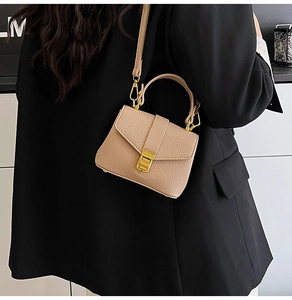 Close-up of litchi pattern beige mini bag with gold metal buckle on black suit jacket
