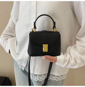 Detail of black lychee grain leather handbag with gold metal clasp and top handle