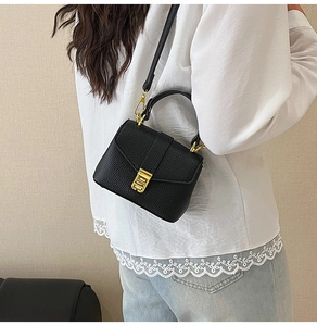 Detail of black lychee grain leather handbag with gold metal clasp and top handle