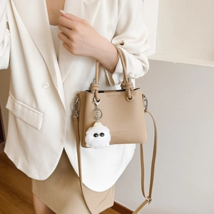 Elegant beige bucket bag with lychee texture and plush charm, worn with white blazer