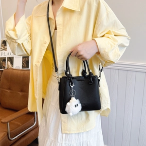 Chic black litchi pattern bucket bag with plush charm shown in a lifestyle side view