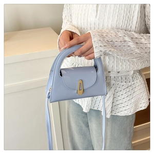 Detail of light blue glossy handbag with golden buckle and integrated curved handle