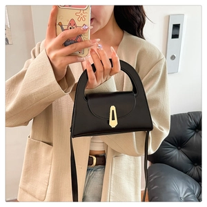 Detail of minimalist black leather handbag with a golden geometric buckle and top handle