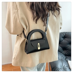 Detail of black semi-circular crossbody bag with golden geometric clasp on female model