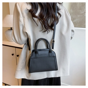 Close-up of black crossbody shell bag showing textured leather and fashion lettering