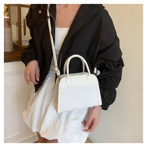 Detailed close-up of a white textured crossbody bag with smooth leather edges and gold hardware