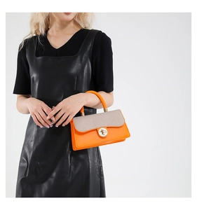 Detail of a bright orange leather handbag with beige textured fabric and gold metal clasp