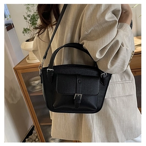 Close-up of black litchi pattern leather bucket bag with metallic buckle on beige blazer