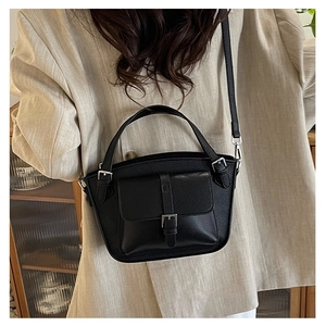 Detail of a black pebbled leather bucket bag styled with a beige blazer for a chic look