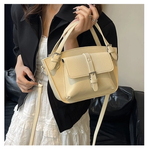Close-up of beige litchi grain leather bucket bag with silver buckle and magnetic flap