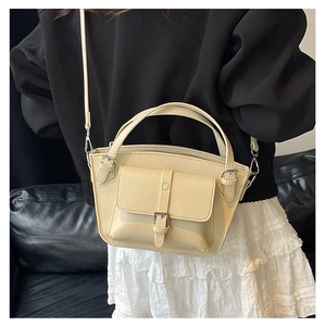 Beige bucket bag shown on a model sitting on a leather sofa with a shoulder strap