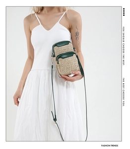 Detail of woven straw phone bag with green leather trim and dual zipper compartments