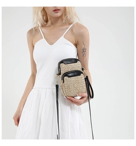 Detail of hand-woven straw crossbody phone bag with black leather trim and gold zippers