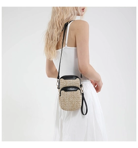 Detail of hand-woven straw crossbody bag with black leather trim on a white dress