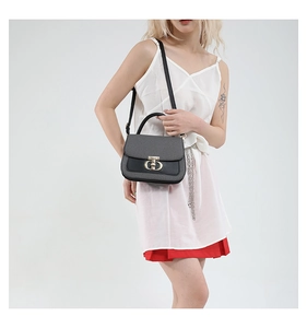 Detailed close-up of textured black handbag with gold oval buckle and top handle