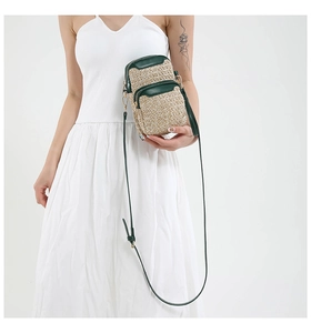 Detail view of woven straw phone bag with dark green leather trim and dual zippers