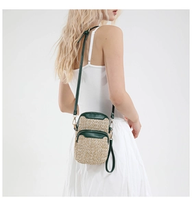 Detail of woven straw crossbody bag with green leather trim and dual zipper texture