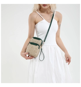 Straw crossbody phone bag with dark green leather trim worn on a white summer dress