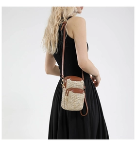 Detail view of woven straw mobile phone bag with brown leather trim and golden zippers