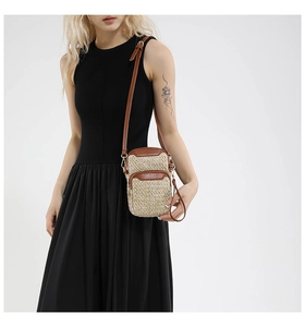 Detail view of woven straw cell phone bag with dual brown leather zipper pockets and strap