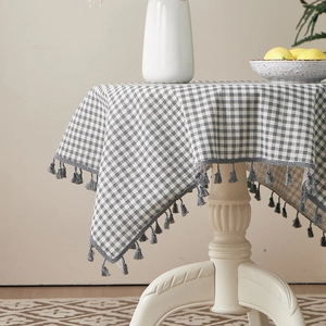 Detail of grey checkered cotton linen tablecloth featuring decorative fringe edges