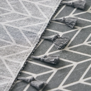 Detail shot of grey geometric arrow pattern tablecloth featuring cotton linen tassels