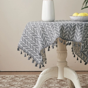 Detail of grey V-pattern tablecloth with tassel fringe on a round wooden coffee table