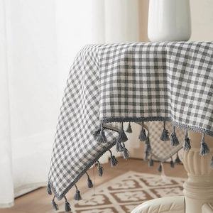 Close-up of gray checkered linen tablecloth with decorative tassel edges on white table