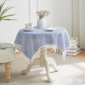 Detail of blue plaid cotton linen tablecloth featuring white tassel edges on a round table