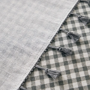 Grey linen tablecloth with tassel edges on a green plaid background for home decor