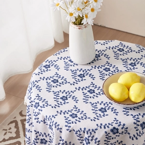 Detail of round cotton linen tablecloth with blue floral pattern and white tassel fringe