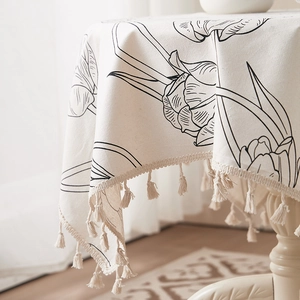 Close-up of beige linen tablecloth with tulip patterns and decorative fringe tassels