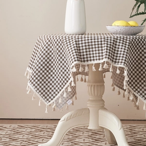 Close-up of brown checkered cotton linen tablecloth with delicate cream fringe tassels
