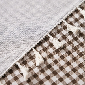 Close-up of grey cotton linen tablecloth with white tassels and plaid pattern detail
